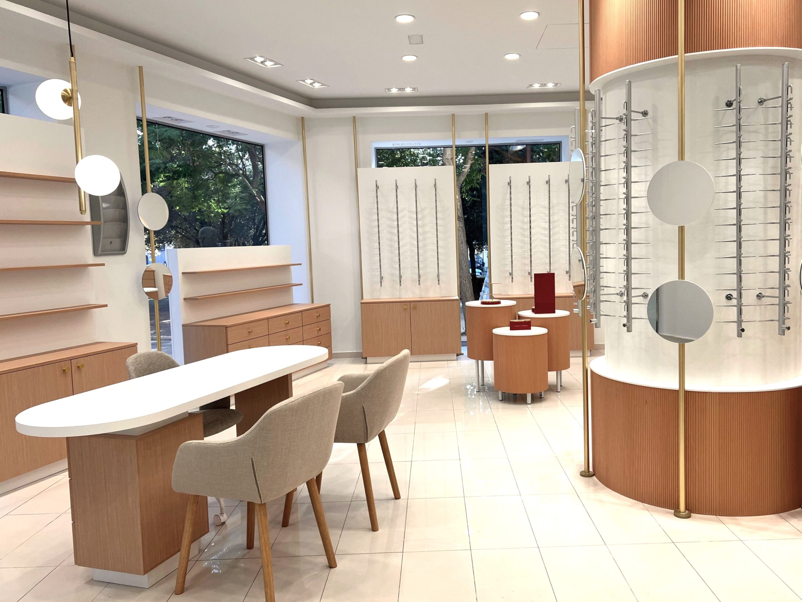 Interior de óptica con expositores cilíndricos, iluminación LED y mobiliario en tonos naturales