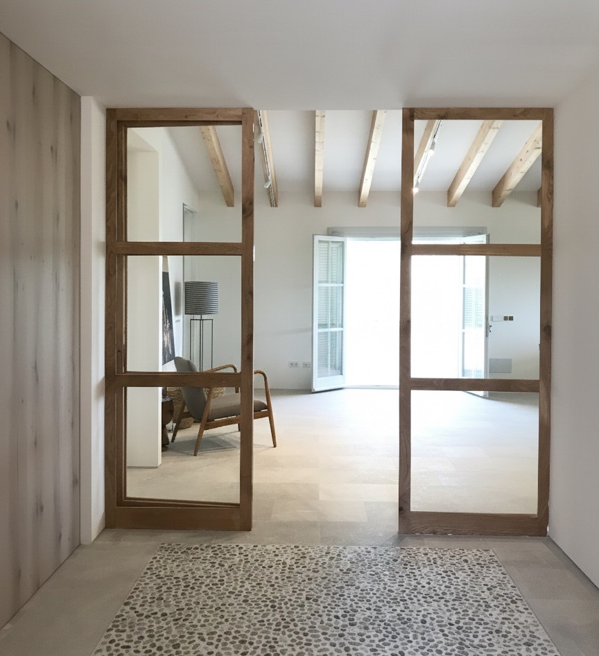 Puertas interiores de vidrio con estructura de madera natural que conectan espacios en vivienda reformada en Mallorca